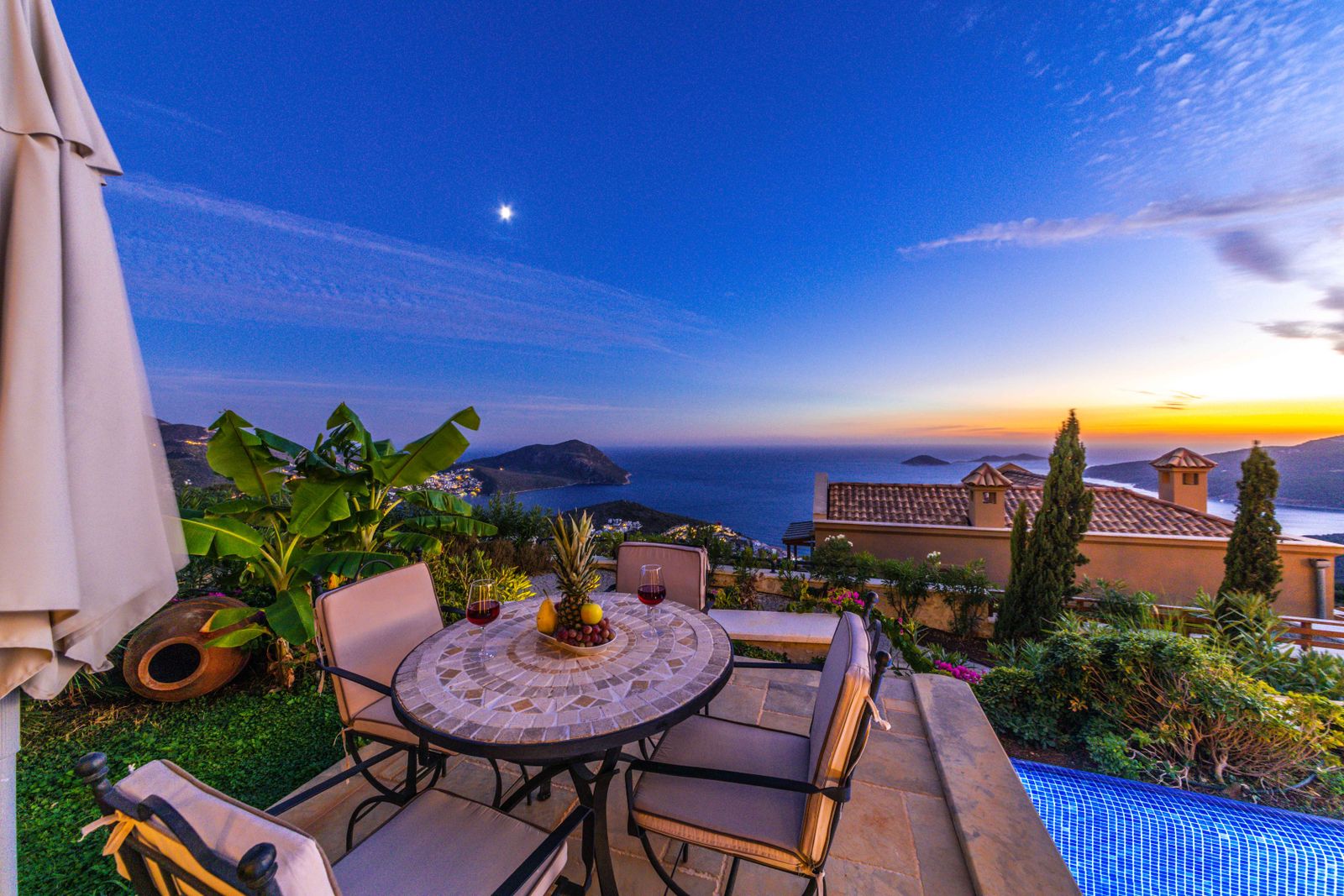 Una terraza de villa mediterránea con mesa de comedor y vista al mar al atardecer