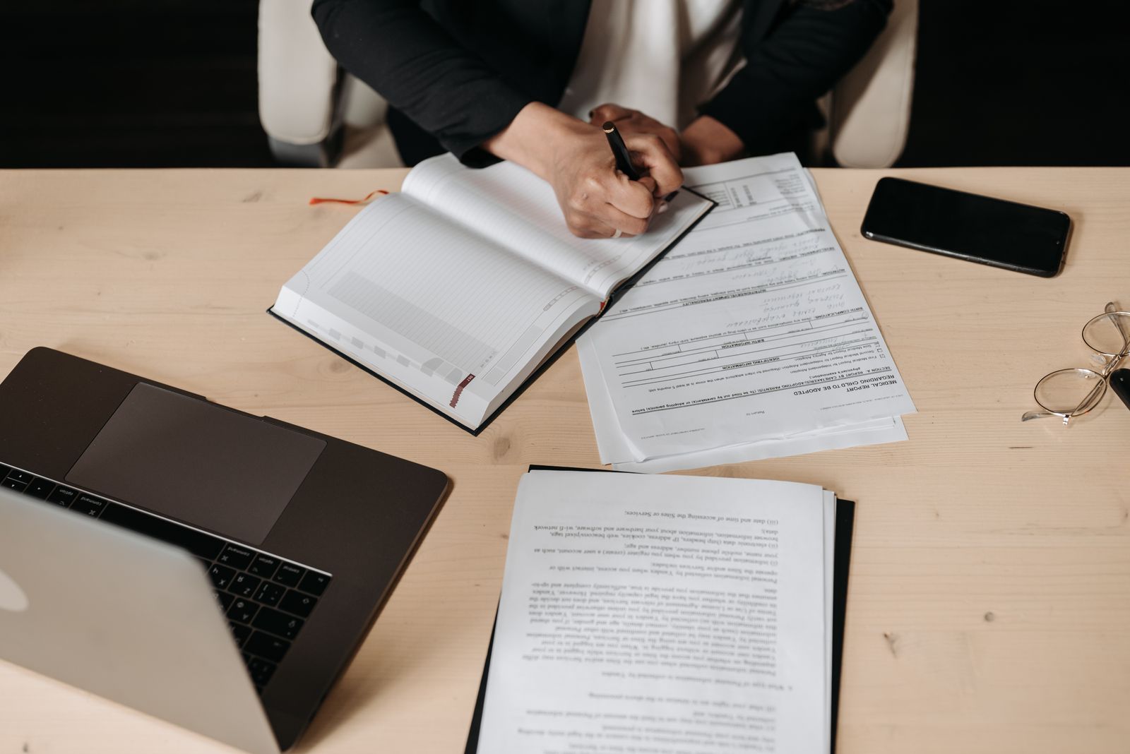 Documents, a notebook and a laptop on a desk during a compliance review