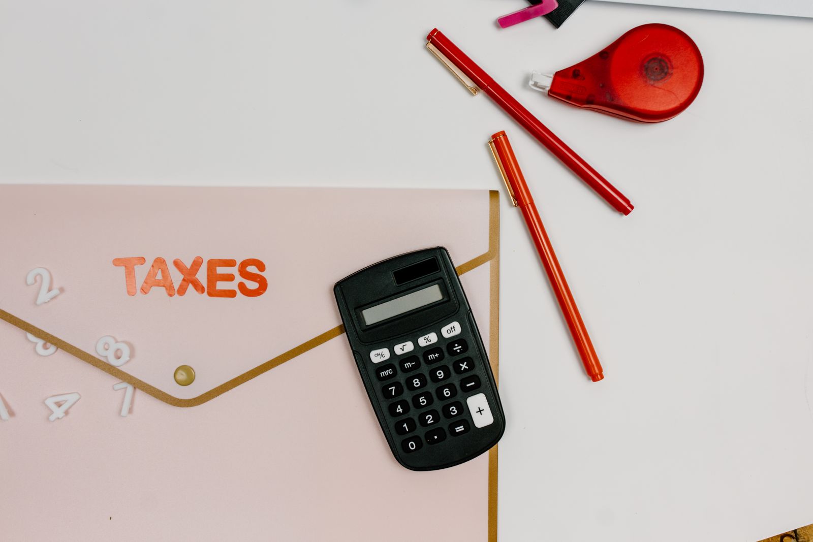 A calculator and pens beside a folder marked Taxes
